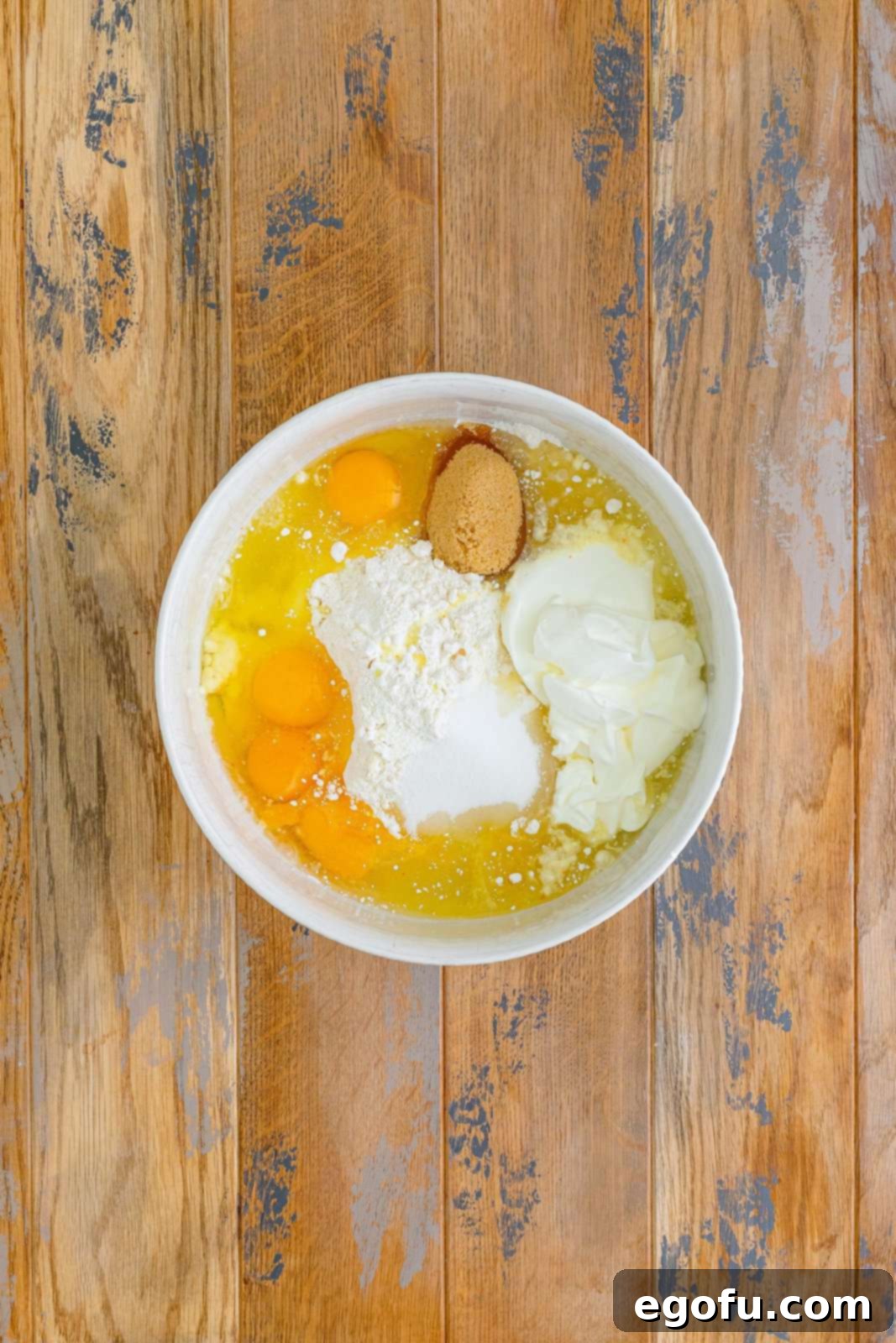 A large mixing bowl with yellow cake mix, sugar, brown sugar, eggs, oil, water, and sour cream.