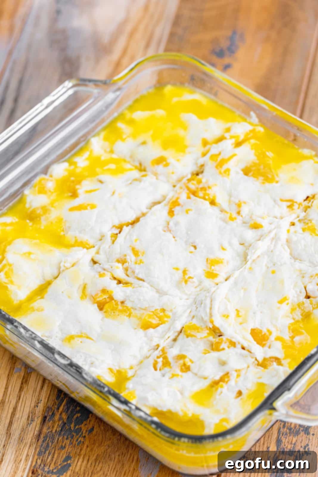 Sun-Kissed Peach Butter Swim Biscuits 10 Unbaked biscuit dough, scored into nine squares, sitting in melted butter in a baking dish.