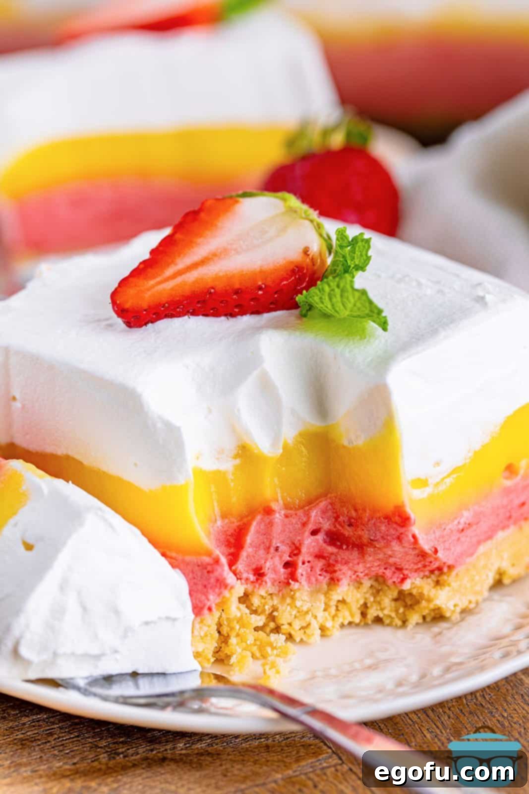 Layered Strawberry Bliss 2 A perfectly sliced piece of Strawberry Lasagna on a white plate, with a small bite taken out, revealing its luscious layers.