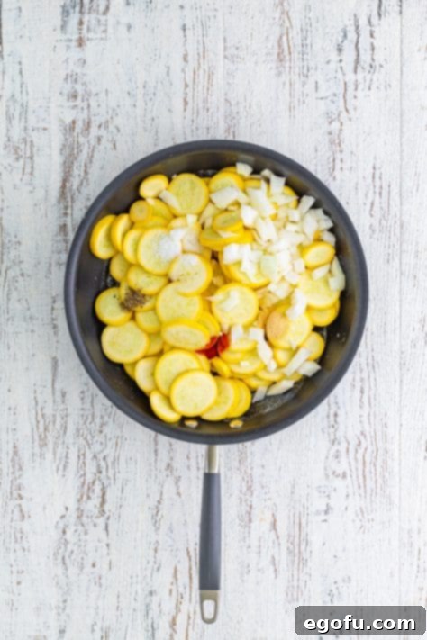 A skillet with melted butter, squash, onion, salt, pepper, garlic powder, and paprika.