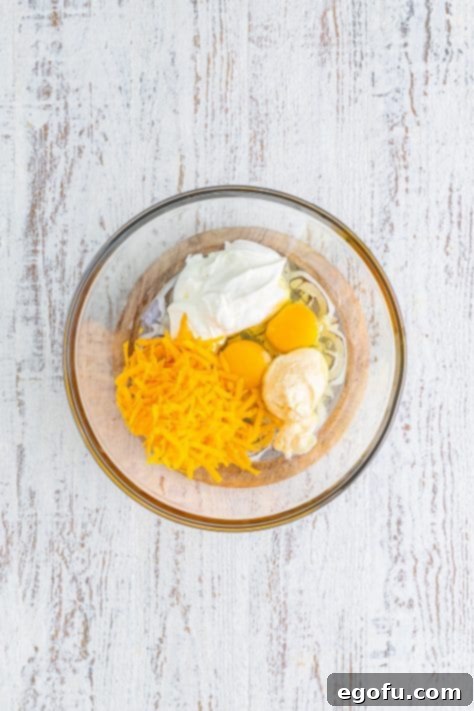 A mixing bowl with eggs, sour cream, mayonnaise, and cheese.