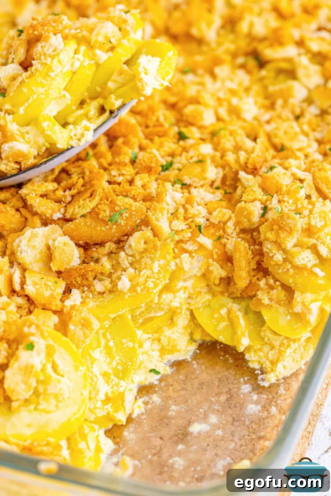 Close up view of the golden brown, bubbly Squash Casserole in a baking dish, with a serving already taken out.