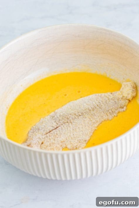 Golden Crispy Catfish 17 Coated catfish fillet in the bowl of egg wash.