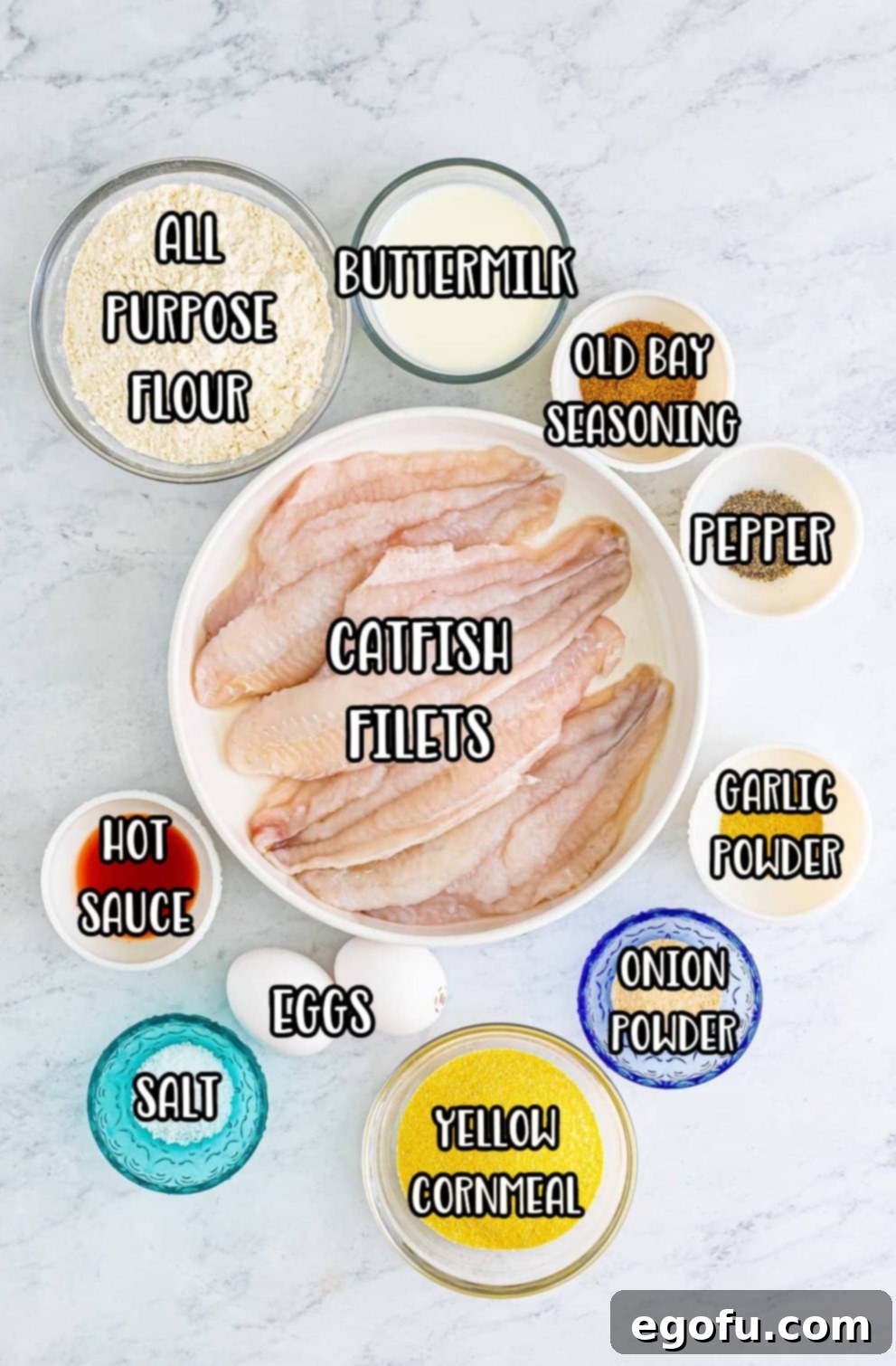Golden Crispy Catfish 4 A vibrant flat lay of all ingredients: catfish fillets, Old Bay seasoning, garlic powder, onion powder, kosher salt, black pepper, all-purpose flour, yellow cornmeal, buttermilk, eggs, hot sauce, and frying oil.