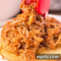 Tongs placing some shredded BBQ chicken on a bun.