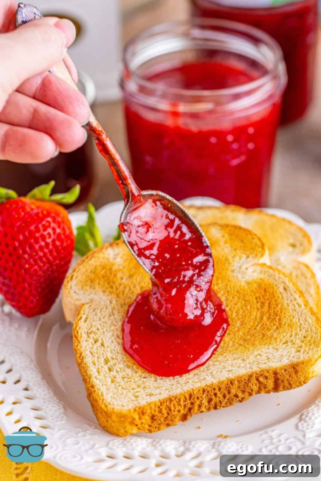 From Garden or Freezer: Homemade Strawberry Jam 2 A hand putting a spoonful of strawberry jam on a piece of toast.