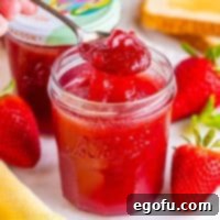 From Garden or Freezer: Homemade Strawberry Jam 12 A jar of homemade Strawberry Jam with a spoon holding some above the jar.