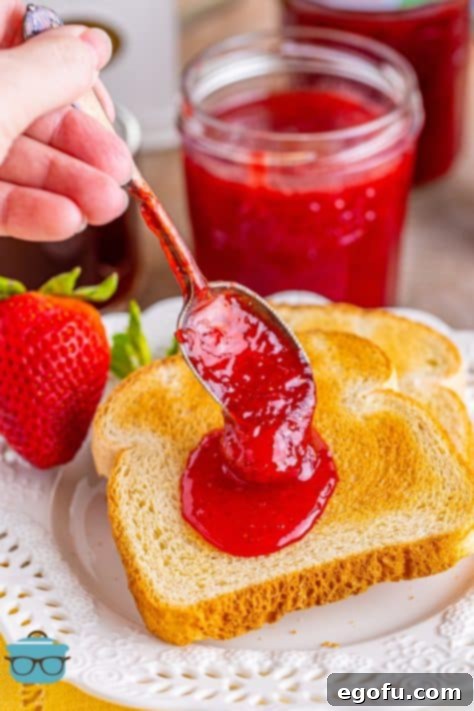 From Garden or Freezer: Homemade Strawberry Jam 18 A hand putting a spoonful of strawberry jam on a piece of toast.