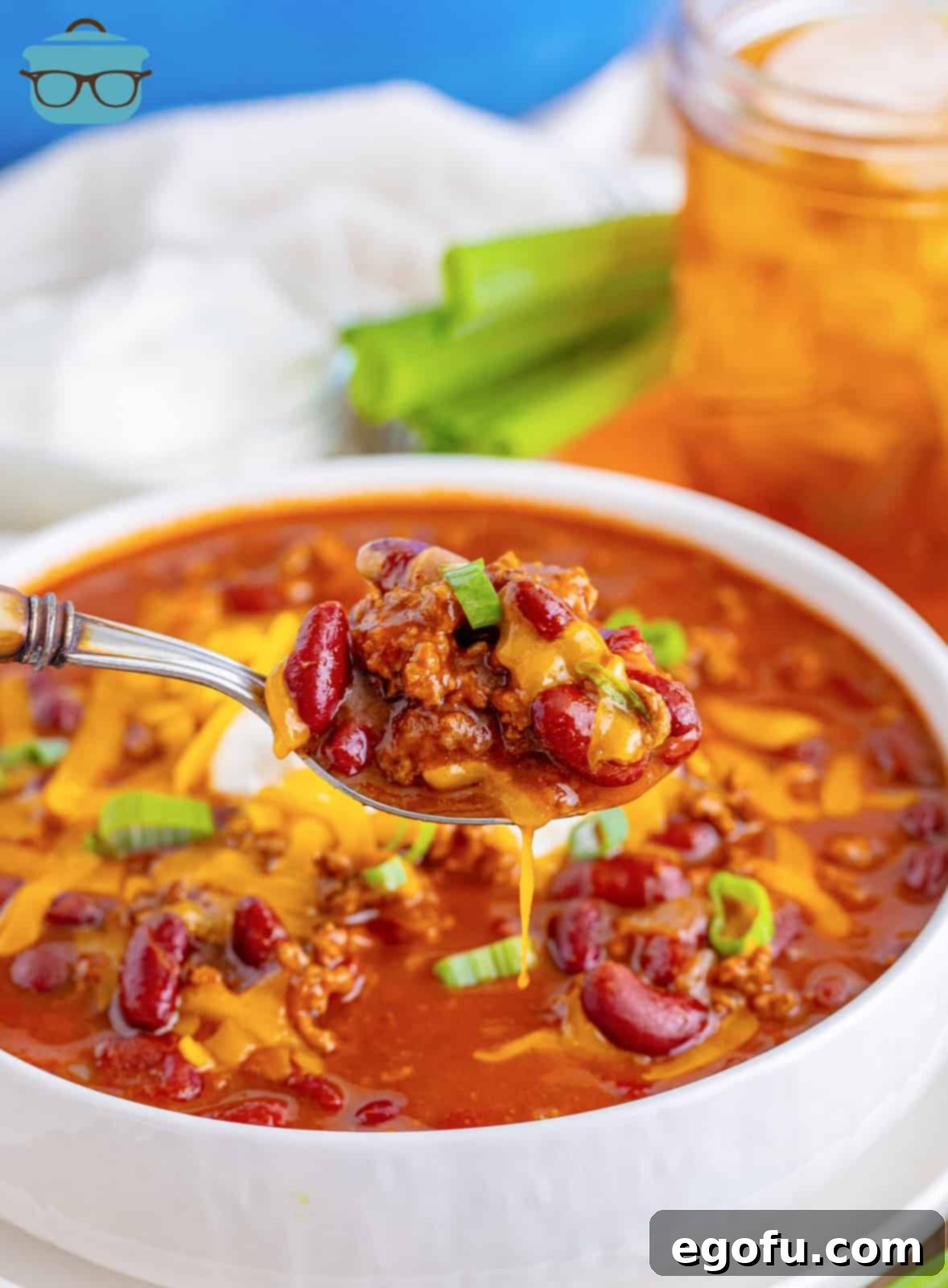 A steaming bowl of classic Cafeteria Chili, garnished with shredded cheese and sour cream, ready to be enjoyed, with a spoon lifting a bite.