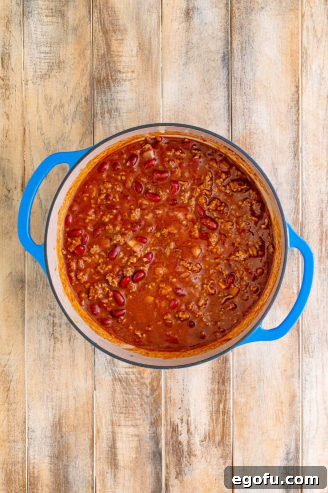 Cafeteria chili gently simmering in a covered Dutch oven, with a slight wisp of steam escaping, indicating it's cooking perfectly.