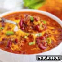 A spoon holding a bite of Cafeteria Chili above a bowl, showcasing its hearty consistency and rich color.