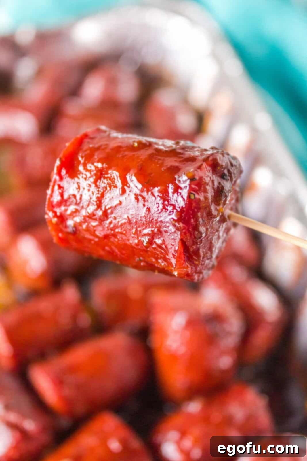 A toothpick holding a hot dog burnt end above a tray, showcasing the glossy sauce.