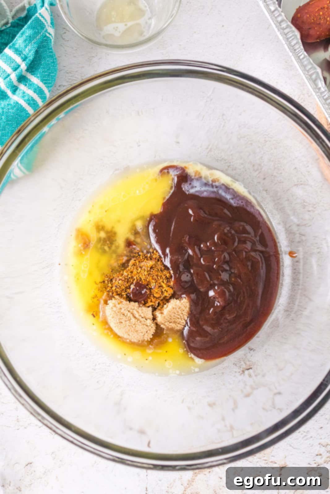 A mixing bowl with BBQ sauce, melted butter, light brown sugar, and BBQ seasoning before mixing.