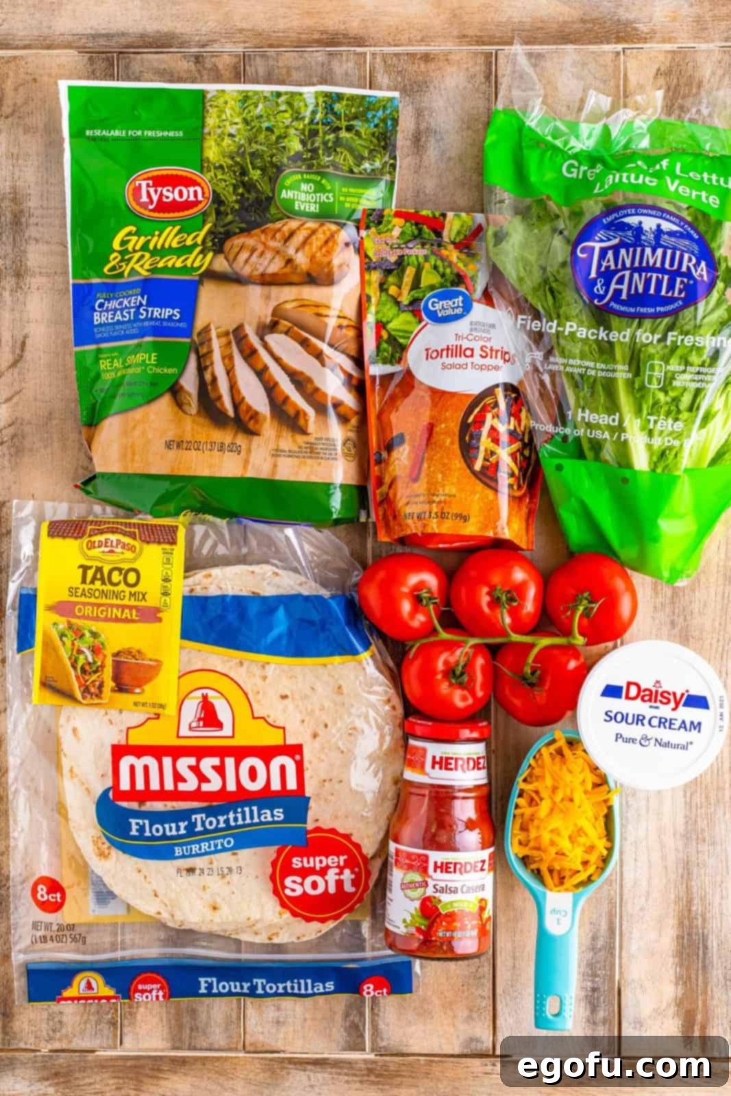 A vibrant flat lay of all the fresh ingredients for Southwest Chicken Wraps, including sour cream, salsa, taco seasoning, chopped lettuce, shredded cheddar cheese, diced tomato, tortilla strips, flour tortillas, and grilled chicken.