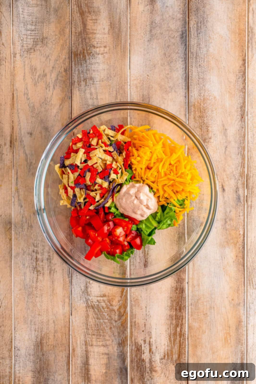 A mixing bowl filled with crisp lettuce, shredded cheese, diced tomatoes, and crunchy tortilla strips, perfectly tossed with a creamy Southwest sauce.