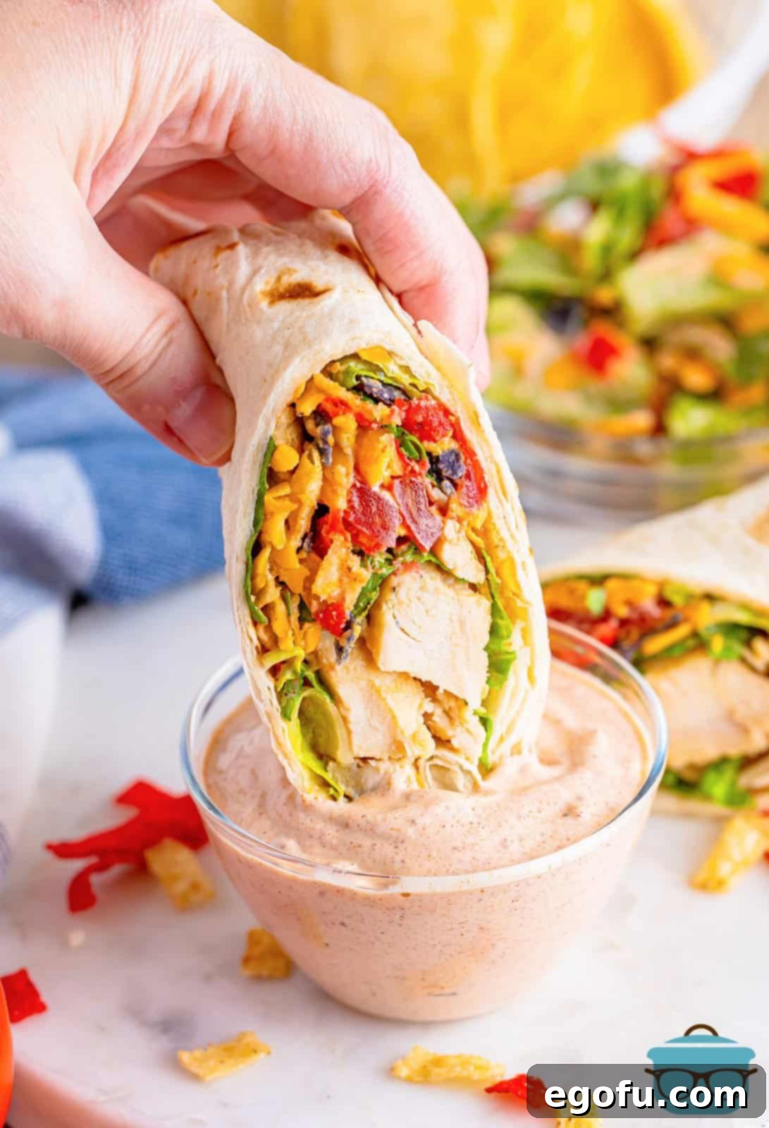 A hand holding a Southwest Chicken Wrap, dipping it into a small bowl of creamy sauce, emphasizing its perfect use as a dippable meal.