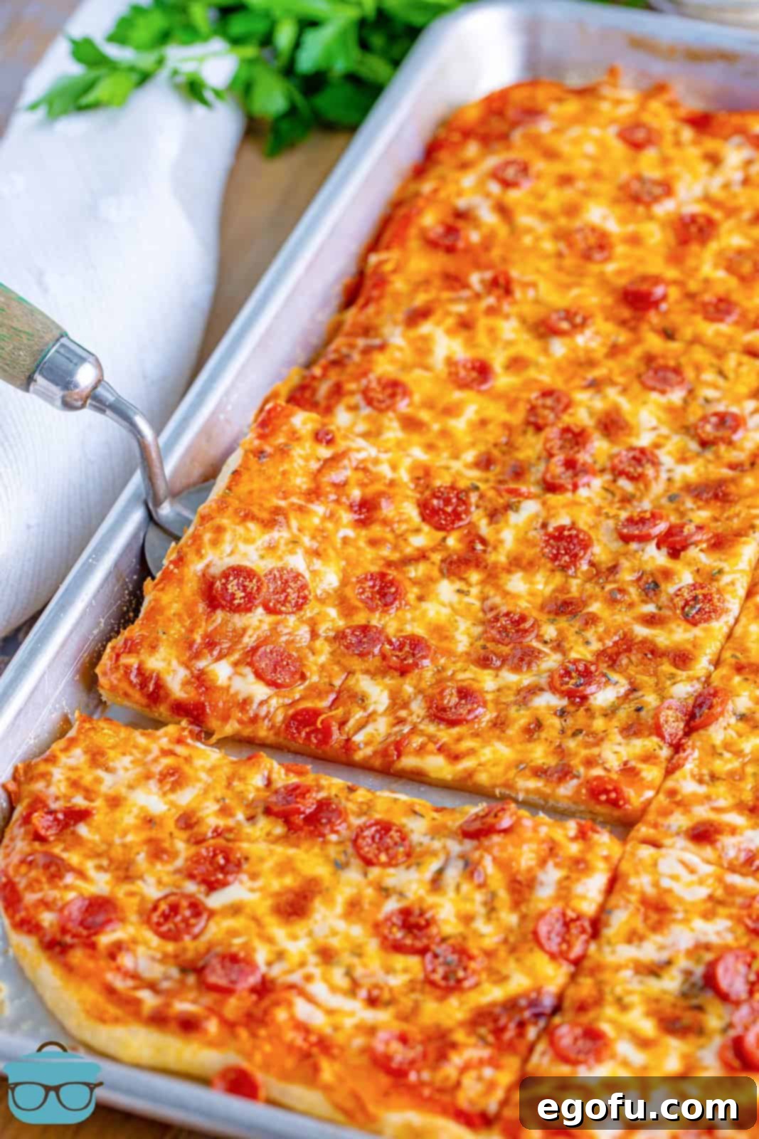 A serving utensil getting ready to pick up a slice of classic Rectangle School Pizza, still warm and inviting.