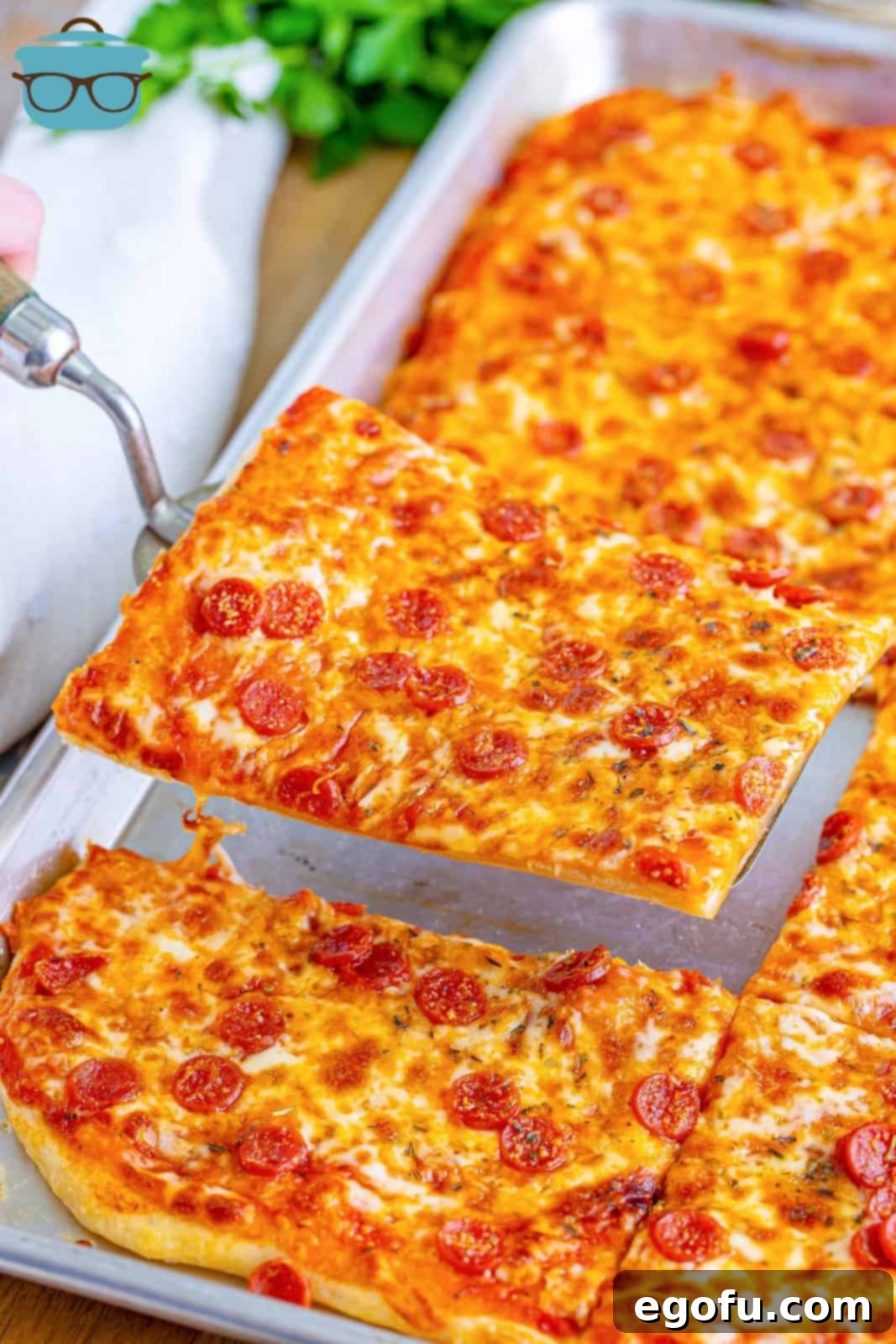 A serving utensil holding a perfectly cut slice of rectangle school pizza, lifted from the pan and ready to be enjoyed.