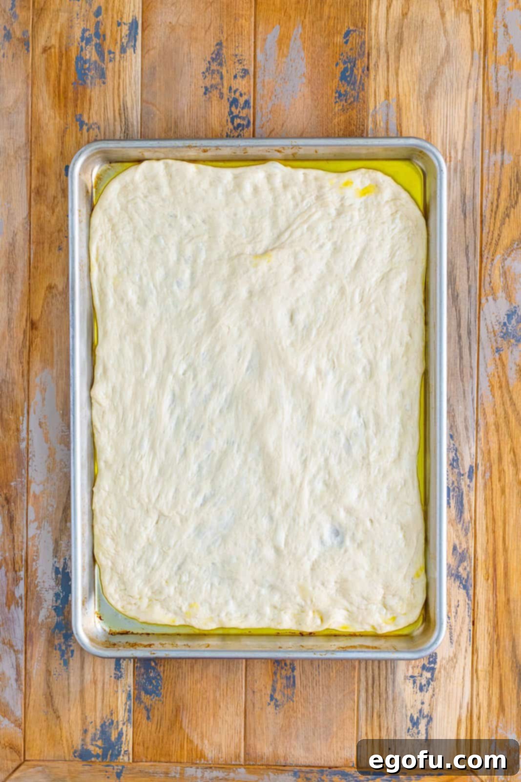 Fresh pizza dough perfectly spread out to cover a large rectangle sheet pan, ready for the next step.