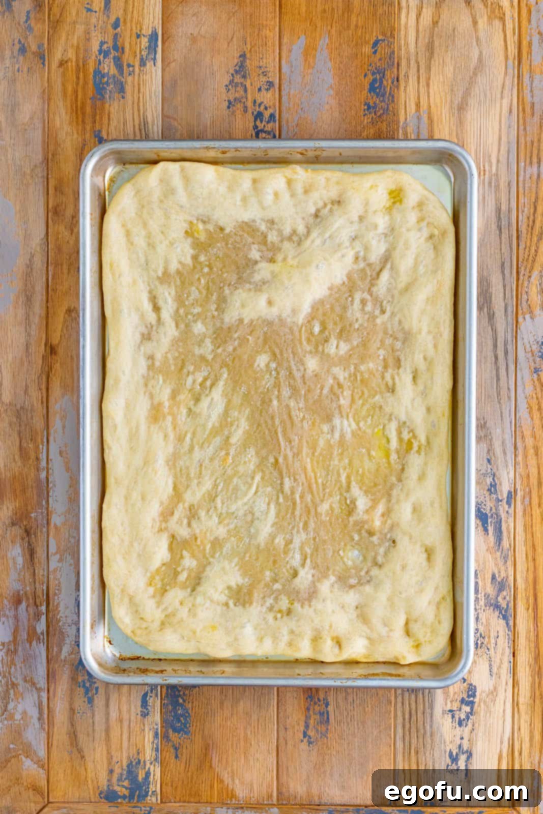 A golden-brown, partially baked pizza crust sitting on a sheet pan, showing a slightly risen and firm texture.