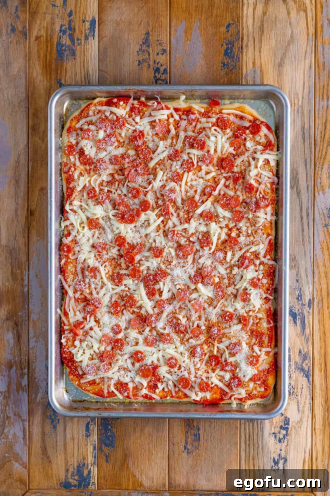 Layers of shredded mozzarella cheese, mini pepperoni, and light seasonings beautifully arranged on top of the pizza sauce and dough.