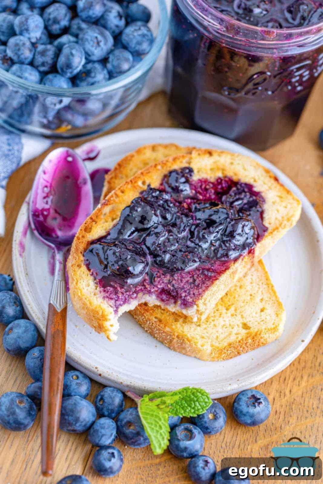 A homemade english muffin with homemade blueberry jam on it.