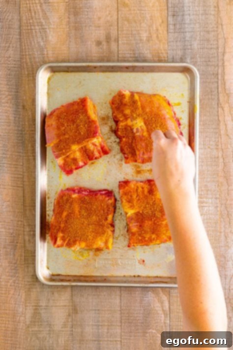 A hand sprinkling bbq seasoning all over rib slabs.