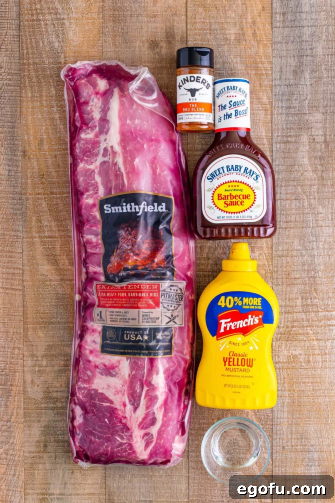 A flat lay image showing all ingredients: ribs, yellow mustard, BBQ sauce, BBQ seasoning, and a small bowl of water.