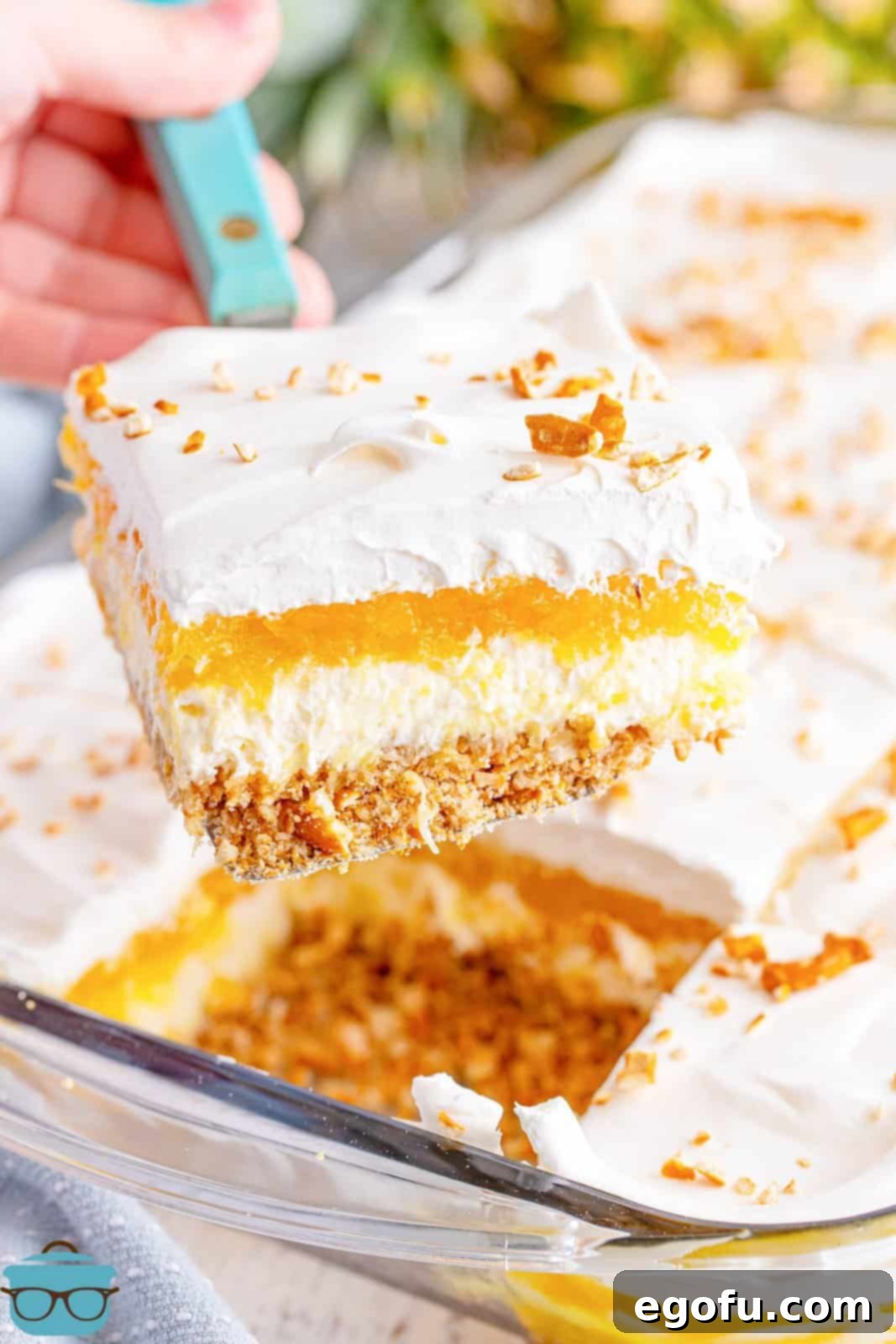 A serving utensil holding a slice of pineapple pretzel salad.
