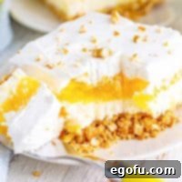 A fork holding a bite of pineapple pretzel salad in front of the rest of the piece of dessert.