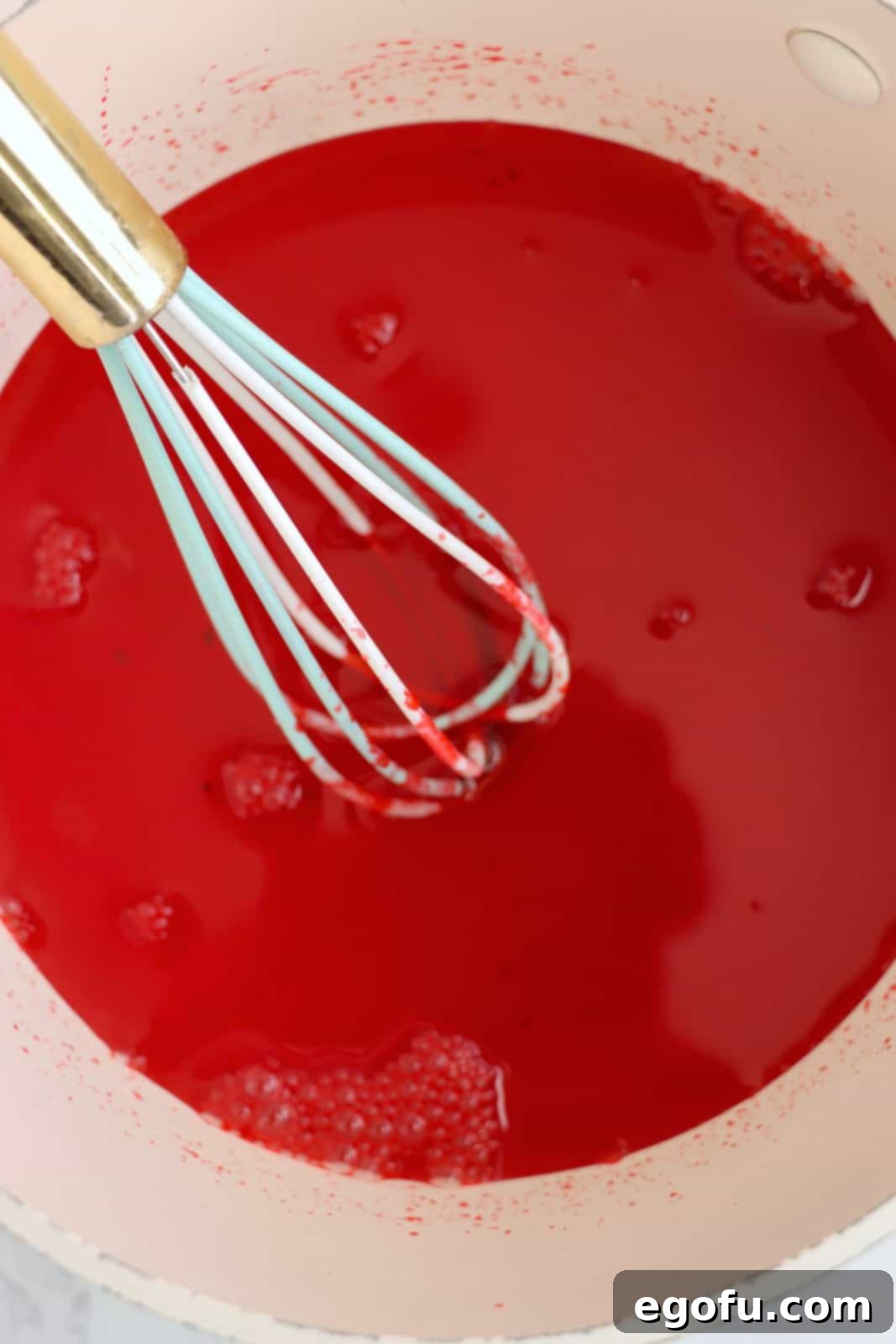 Festive Tri-Color Jell-O Cups 6 Cherry jello mixture in a bowl with a whisk, ready for cooling.