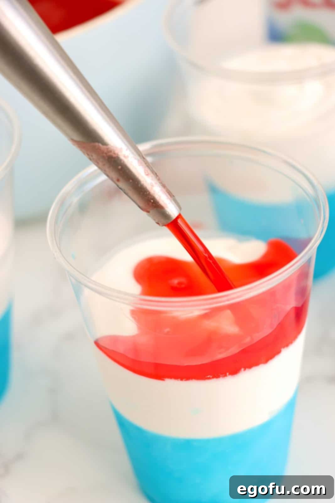 Festive Tri-Color Jell-O Cups 9 A turkey baster carefully pouring red jello on top of the white whipped cream and blue jello layers.