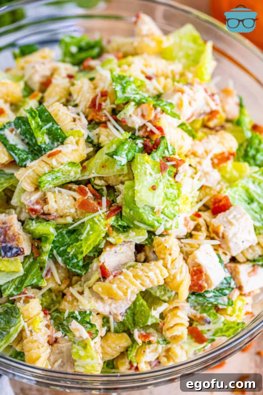 Delicious chicken Caesar pasta salad in a clear glass bowl, showcasing fresh romaine, pasta, chicken, and bacon.