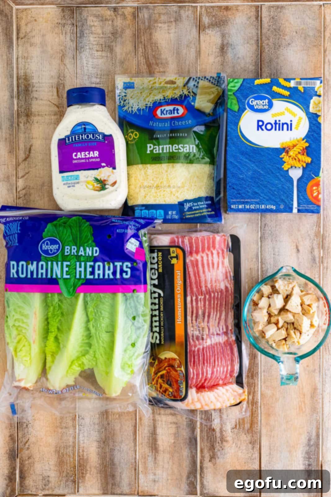 All six key ingredients laid out: rotini pasta, diced grilled chicken, crispy bacon, fresh romaine lettuce, shredded Parmesan, and Caesar dressing.