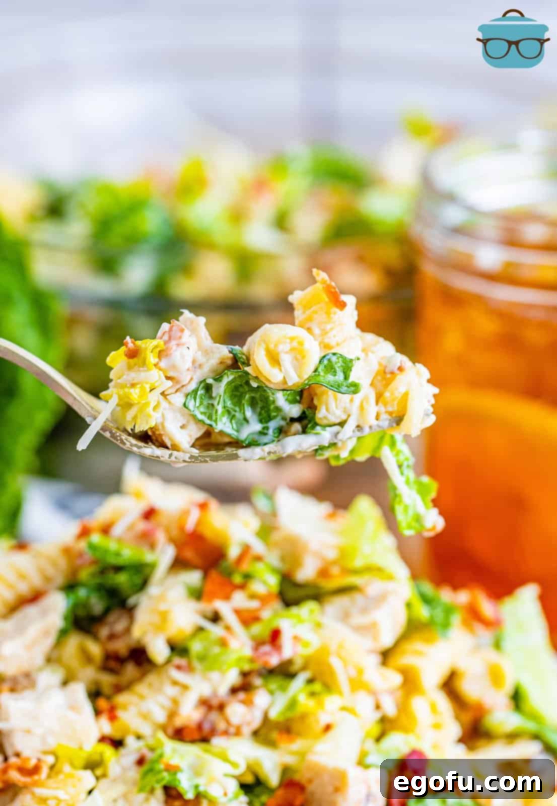 Close-up of a fork lifting a perfect bite of Chicken Caesar Pasta Salad, showing pasta, chicken, bacon, and lettuce.