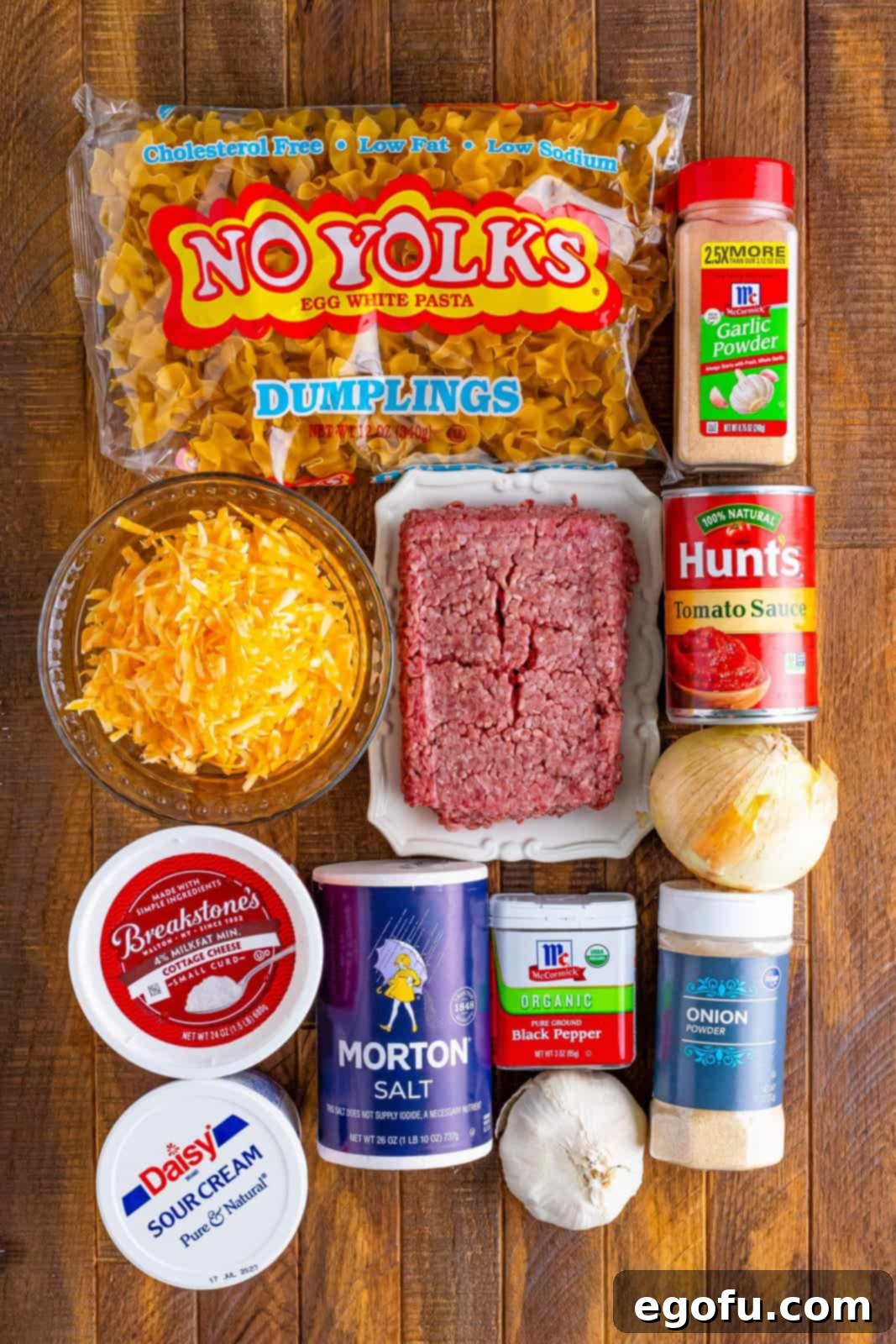Creamy Baked Noodle Delight 4 A flat lay image showing all the raw ingredients for Sour Cream Noodle Bake: ground beef, onion, garlic, tomato paste, salt, pepper, egg noodles, cottage cheese, sour cream, garlic powder, onion powder, and shredded Colby Jack cheese.