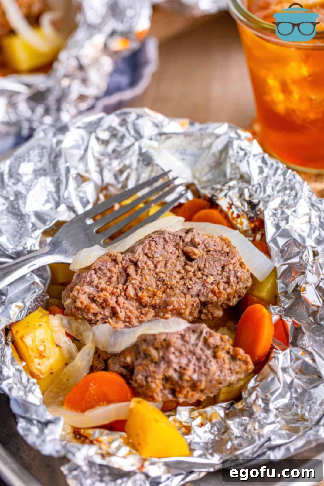 Aluminum foil packet with a burger patty, potatoes and carrots.