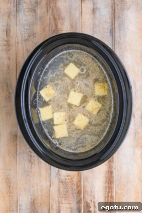 Grits, water, salt, butter, and black pepper in a crock pot, ready for slow cooking.