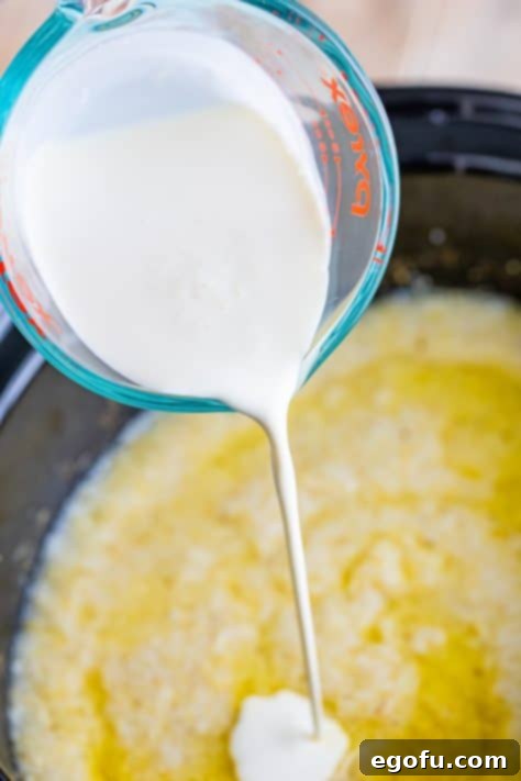 Heavy cream being poured into the cooked grits, ready to be stirred.