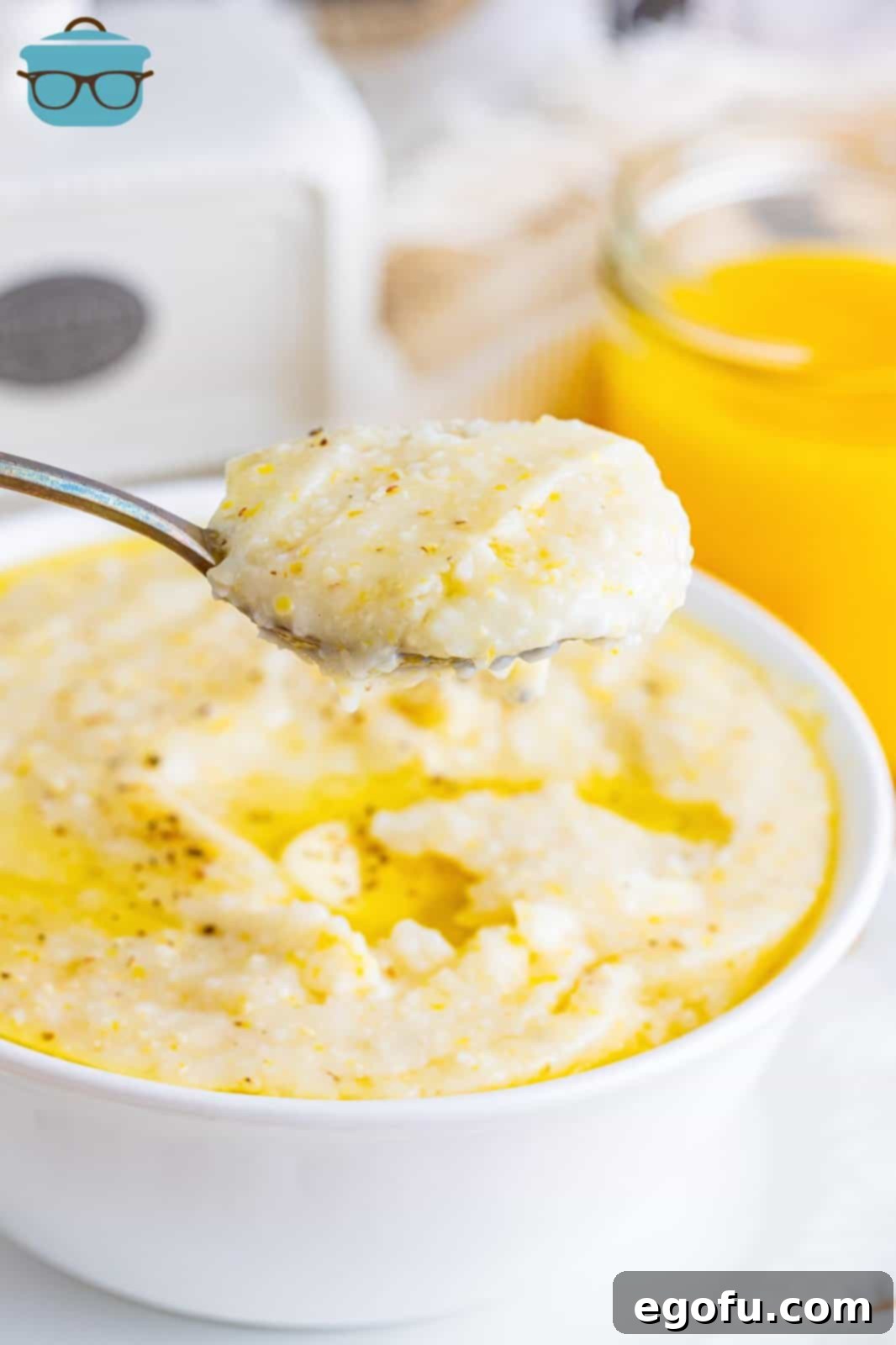 A bowl of southern grits with a spoon holding a bite above it, garnished with a pat of melting butter.