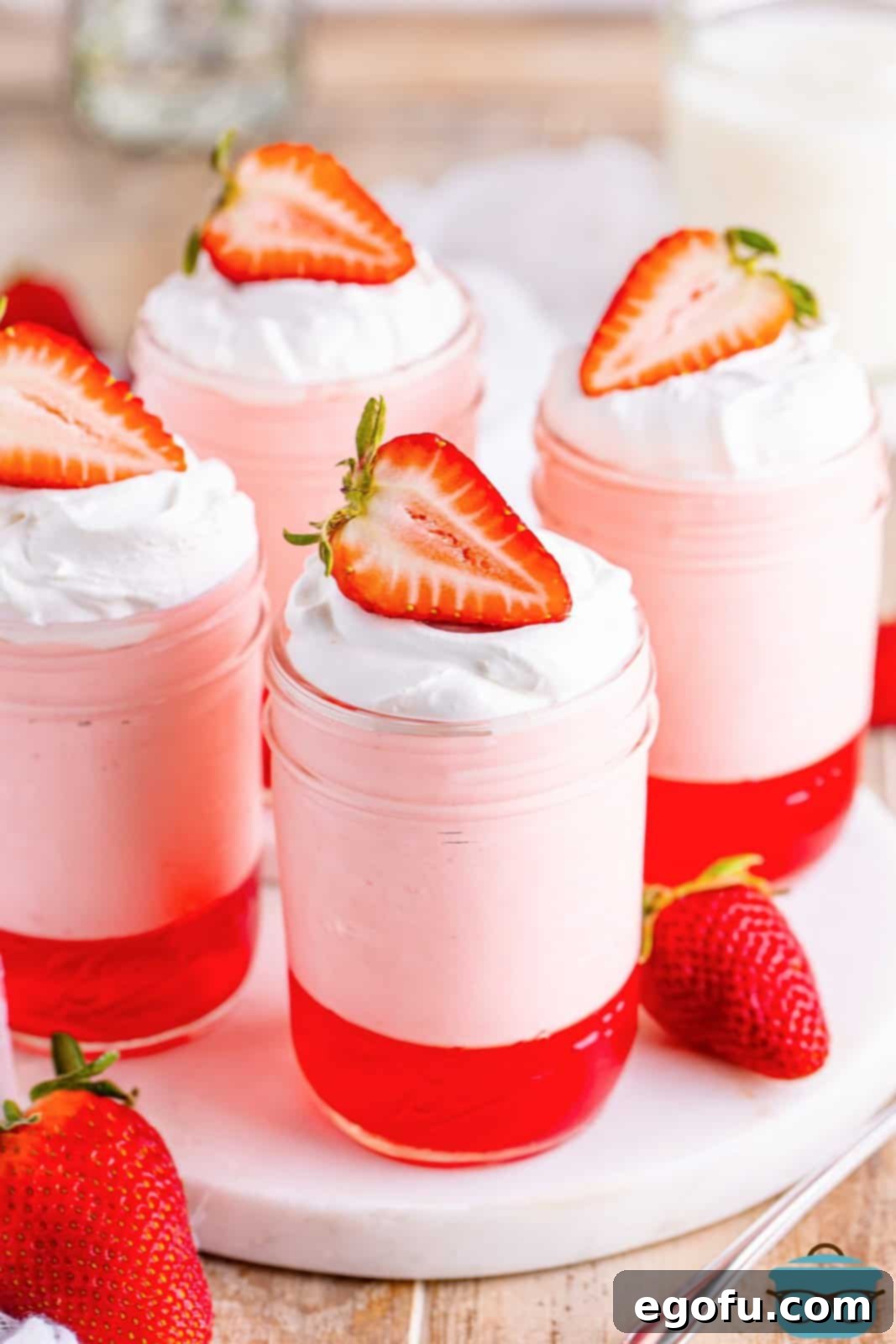 Four jars of strawberry Jell-O parfait with strawberries on top.