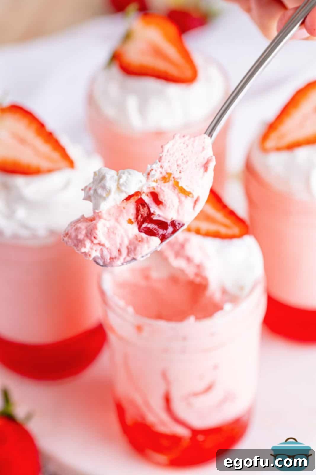 A spoon holding a bite of a strawberry Jell-O parfait.
