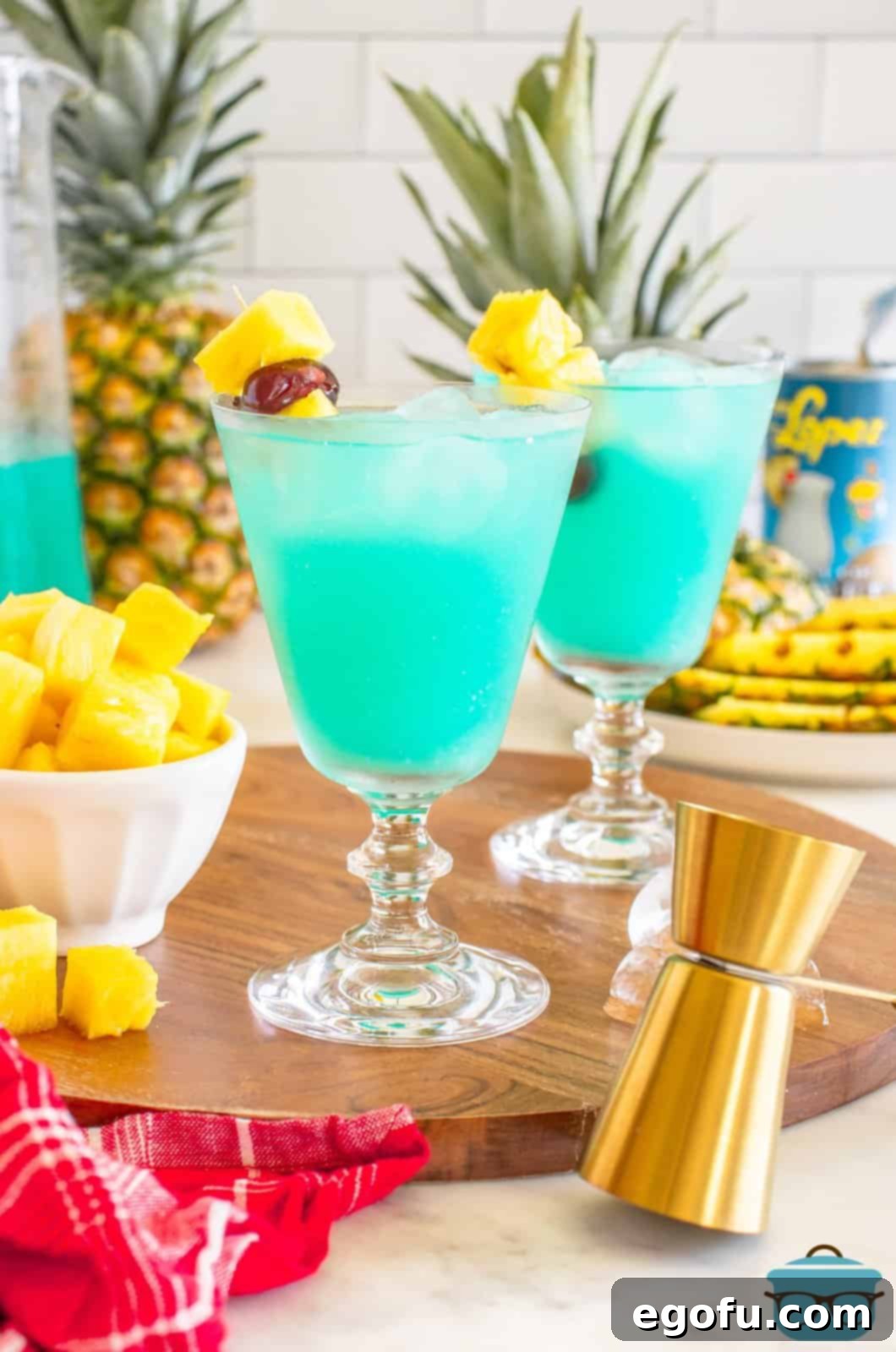 Two Blue Hawaiian cocktails with garnishes of pineapple and cherries, set against a blurred tropical background.