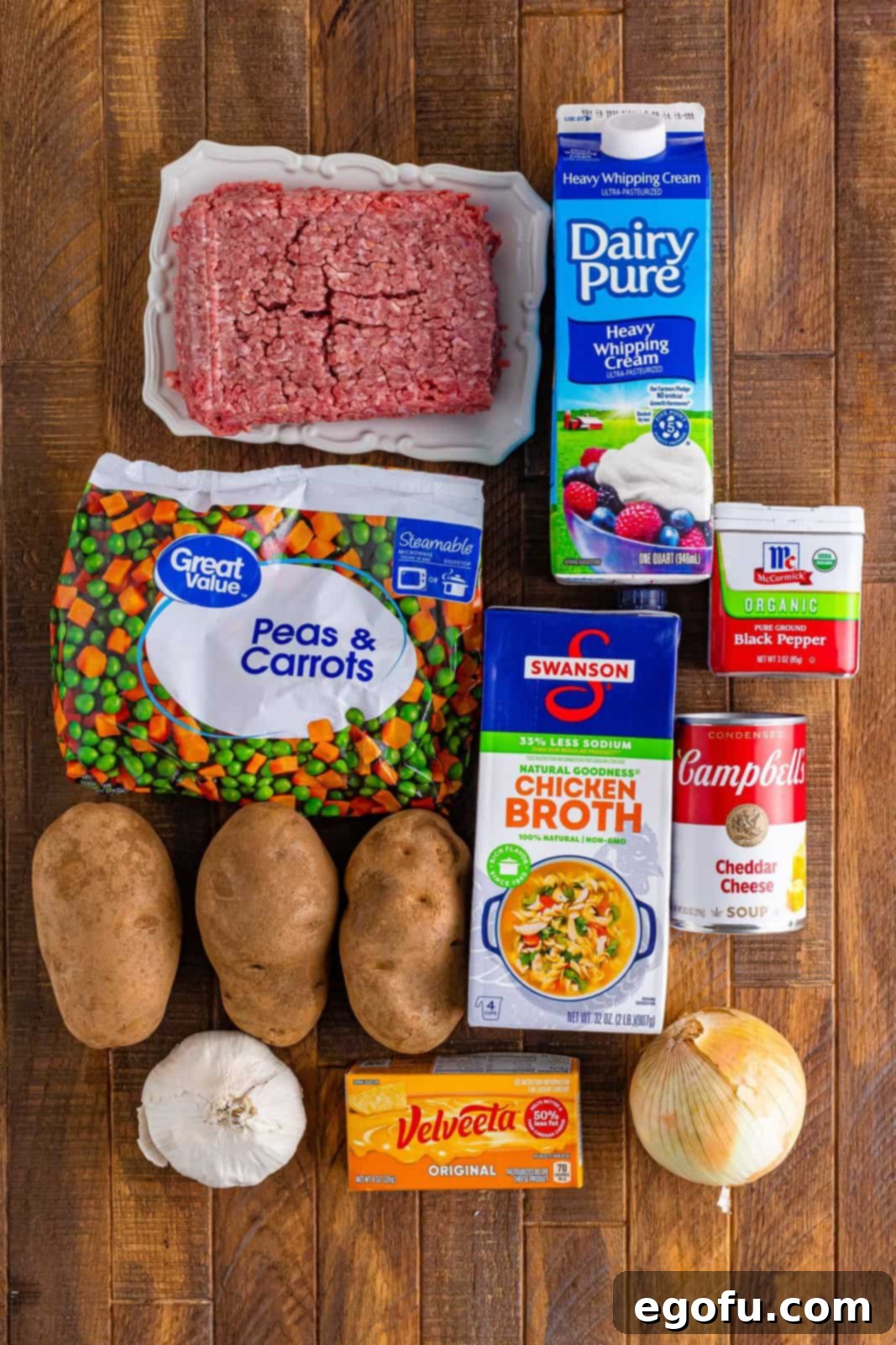 Ground beef, peas and carrots, potatoes, Velveeta, onion, garlic, cream of cheddar soup, black pepper, and heavy cream laid out as ingredients.