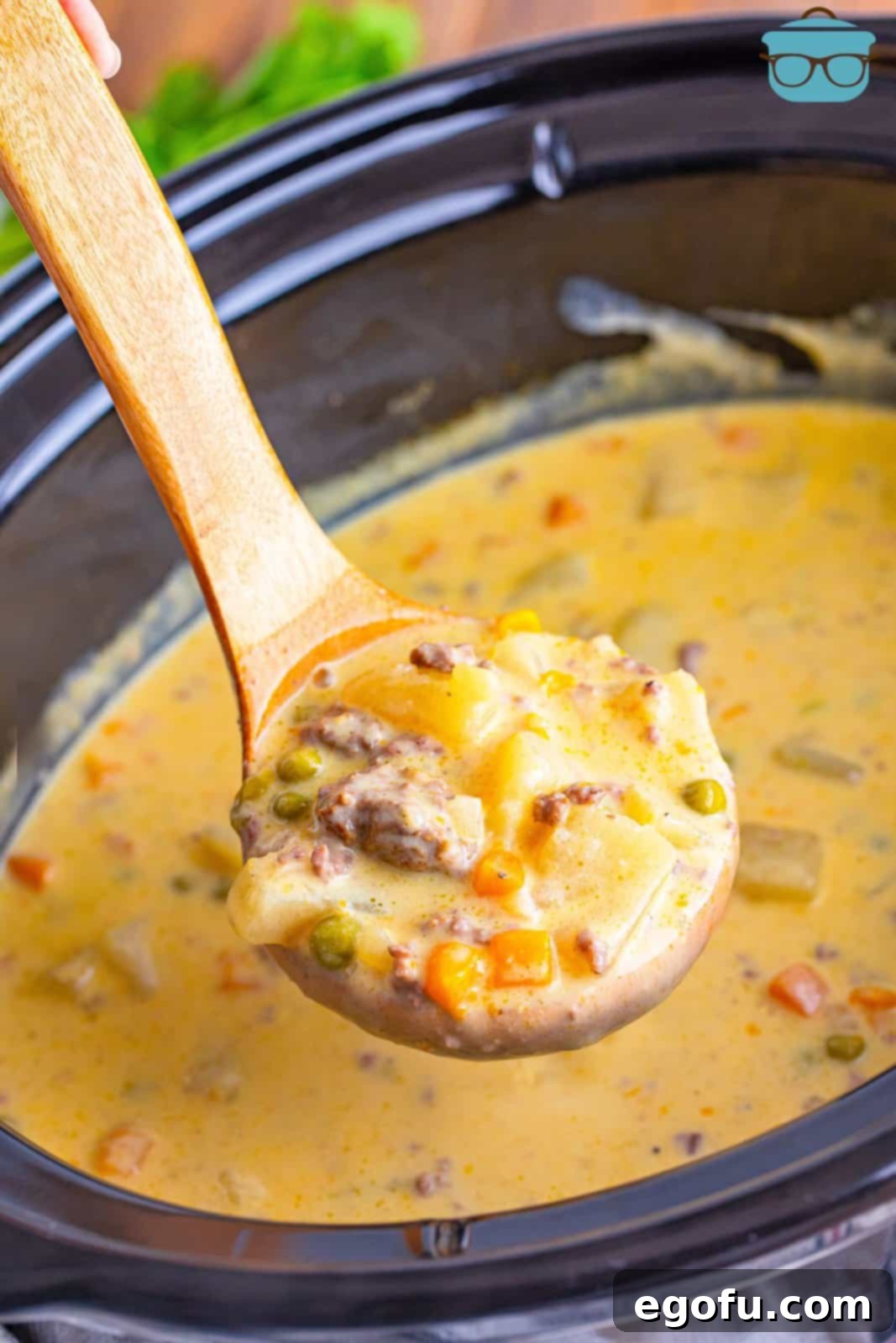 A ladle holding some Hamburger Potato Soup above a Crockpot, ready to serve.