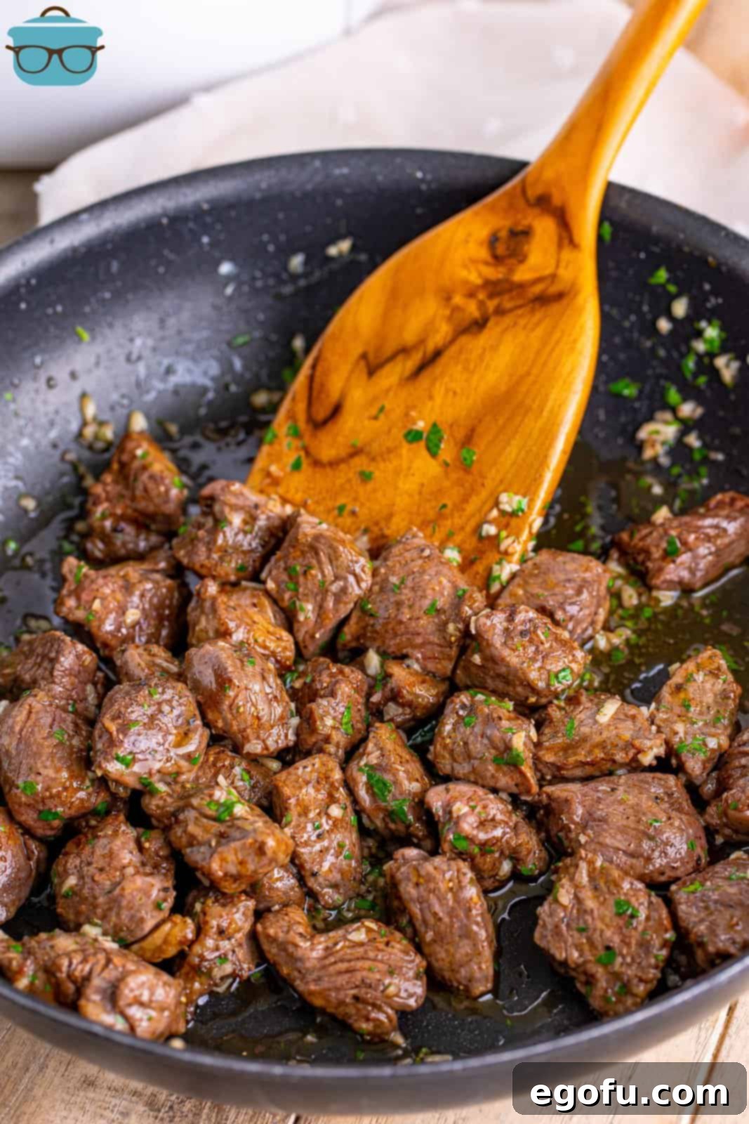 A skillet with Air Fryer Garlic Butter Steak Bites and a wooden spatula.