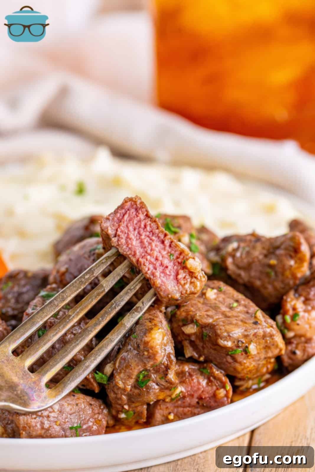 A fork holding a bite of Air Fryer Garlic Butter Steak Bites above a plate with the rest.