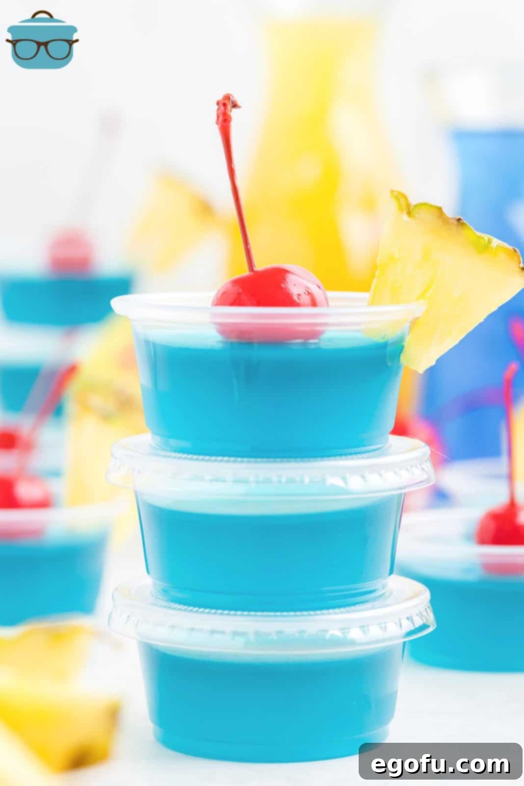 A stack of vibrant blue Jell-O shots, garnished with small pineapple wedges and maraschino cherries, ready for a tropical party.