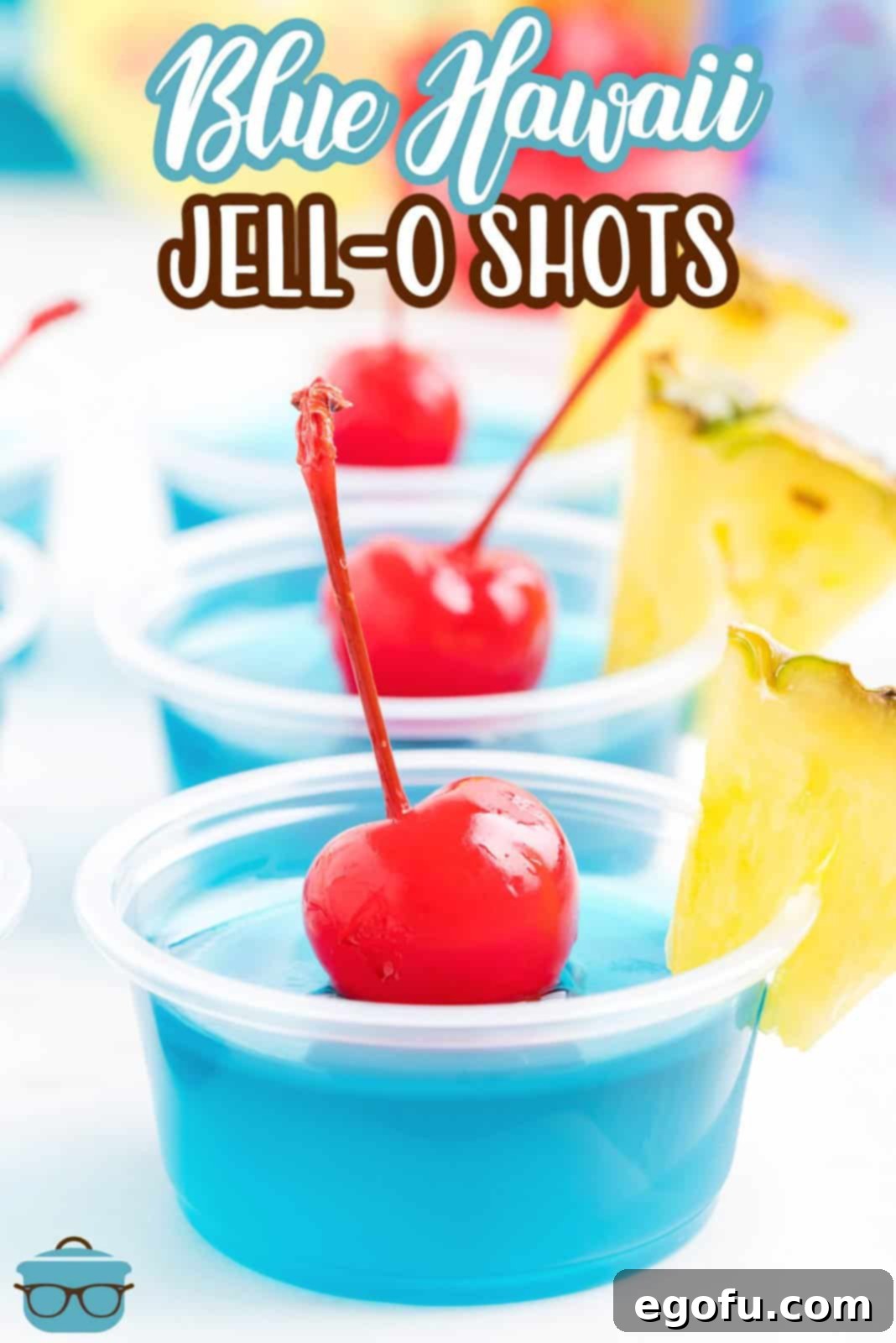 Two Blue Hawaii Jell-O Shots, beautifully garnished with pineapple wedges and maraschino cherries, on a white surface.