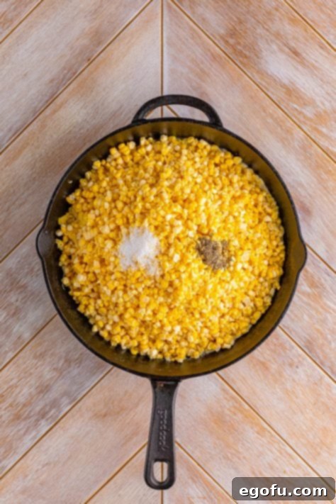 Butter, salt, pepper, and corn in a cast iron skillet, ready to be stirred.